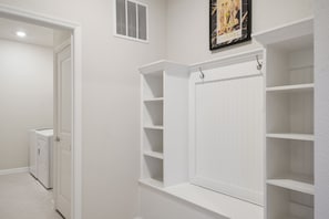 A hallway with a built-in shelving unit, a door leading to a laundry area, and a vent on the wall. - Family Fun Villa: Themed Rooms, Private Pool & Spa (Clermont)
