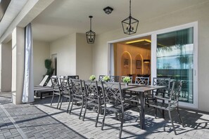 An outdoor patio with a dining area featuring metal chairs and tables, a glass door leading inside, and hanging lantern-style lights. - Family Fun Villa: Themed Rooms, Private Pool & Spa (Clermont)