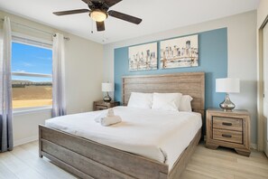 Un dormitorio con cama, mesita de noche, ventilador de techo y obra de arte en la pared.