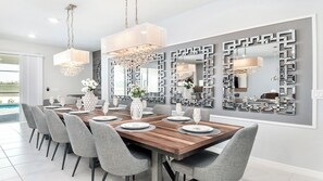A modern dining room with a wooden table set for six, grey upholstered chairs, and a large mirror with geometric patterns on the wall. - 9br/star Wars/harrypotter Themed Rooms/pool/disney (Davenport)