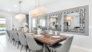 A dining area with a wooden table set for six, grey upholstered chairs, and a large wall mirror with geometric patterns. - 9br/star Wars/harrypotter Themed Rooms/pool/disney (Davenport)