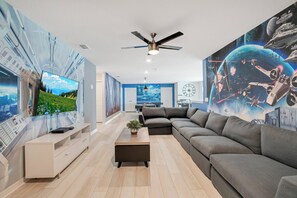 A modern living room with a large sofa, a coffee table, and a flat-screen TV. - 9br/star Wars/harrypotter Themed Rooms/pool/disney (Davenport)