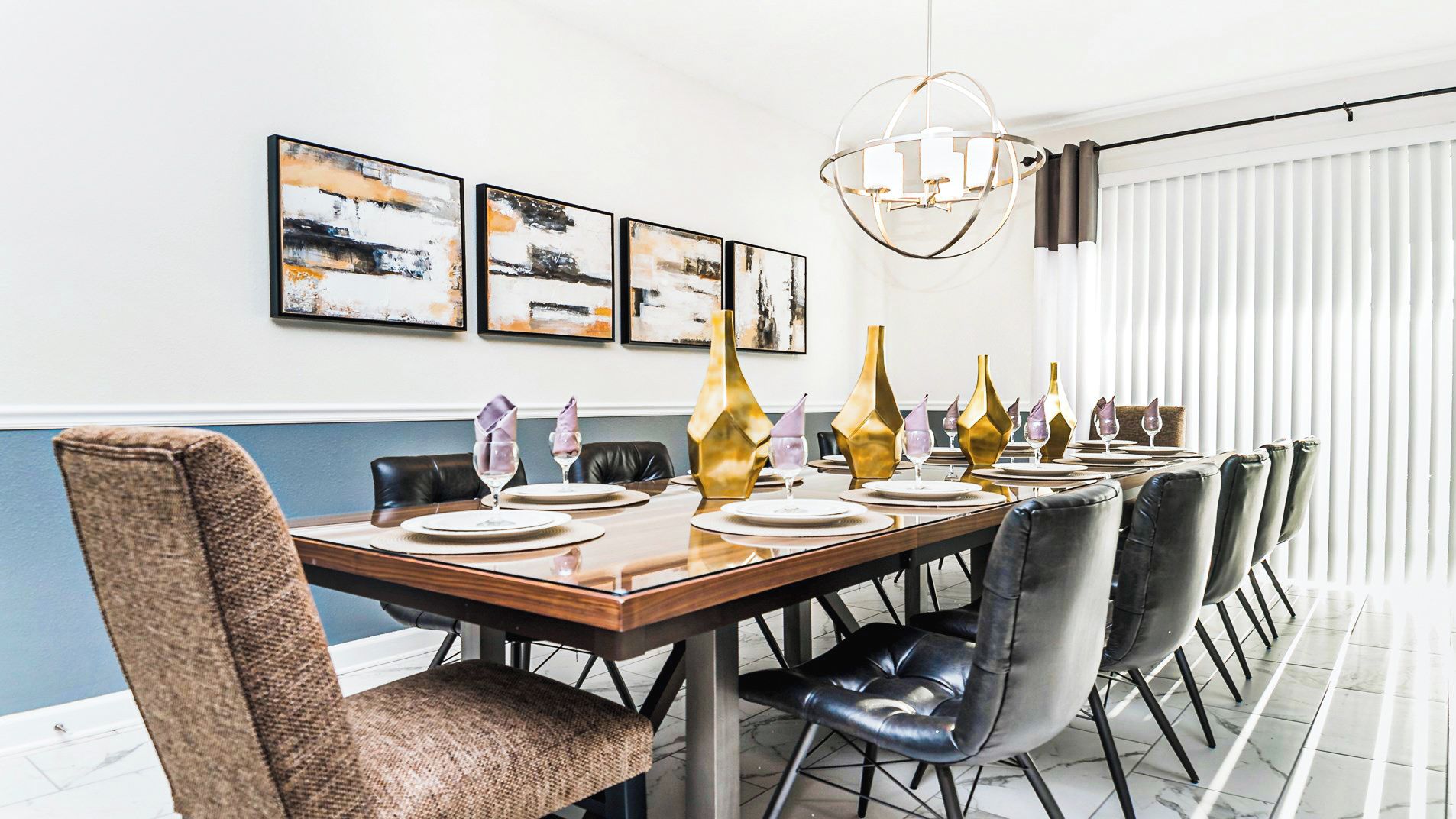 Comedor con una larga mesa dispuesta para seis, que cuenta con una lámpara moderna, arte abstracto en la pared y vistas al exterior a través de amplios ventanales.