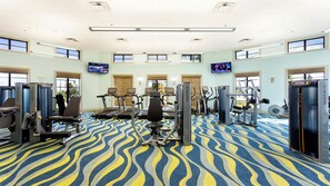 Une salle de sport spacieuse, dotée de divers appareils d’exercice, de grandes fenêtres et d’un tapis à motifs.