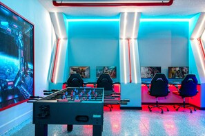 Ein Raum mit einem Kicker, zwei Gaming-Stühlen und einem großen Bildschirm, der ein Videospiel zeigt.