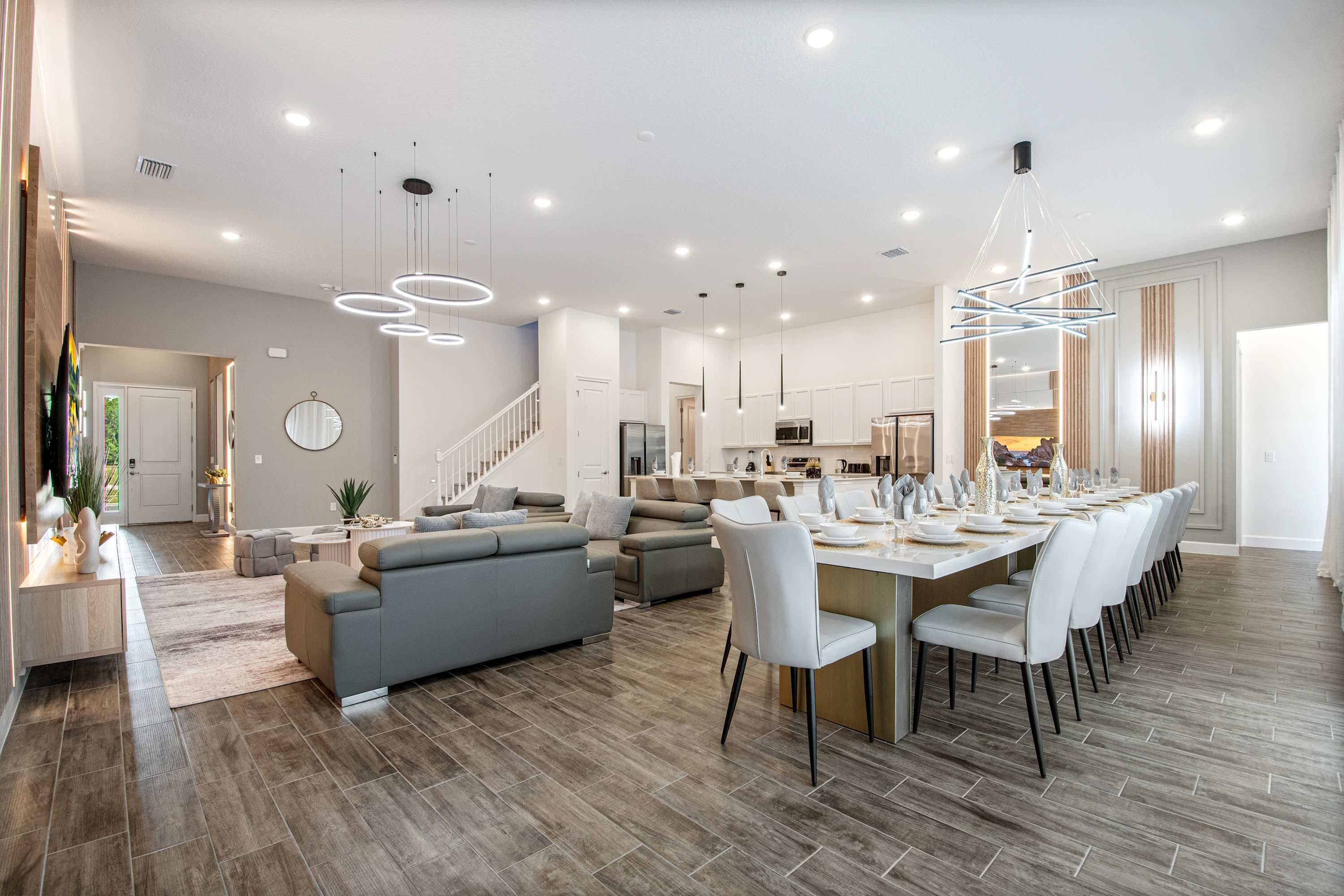 Amplia sala de estar con cocina moderna, comedor con una mesa larga y una escalera que conduce a un piso superior.