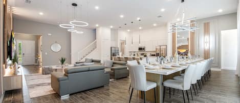 Amplia sala de estar con cocina moderna, comedor con una mesa larga y una escalera que conduce a un piso superior.