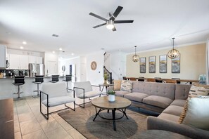 A modern living room with a sofa, chairs, a coffee table, and a kitchen in the background. - Games/themed Rooms/greenview/ 9BR @ Storeylake! (Kissimmee)