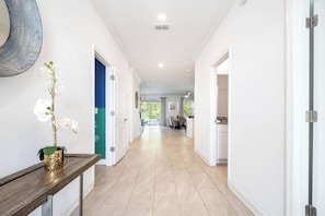 A hallway with a wooden console table, white walls, and a view into a kitchen area. - Games/themed Rooms/greenview/ 9BR @ Storeylake! (Kissimmee)