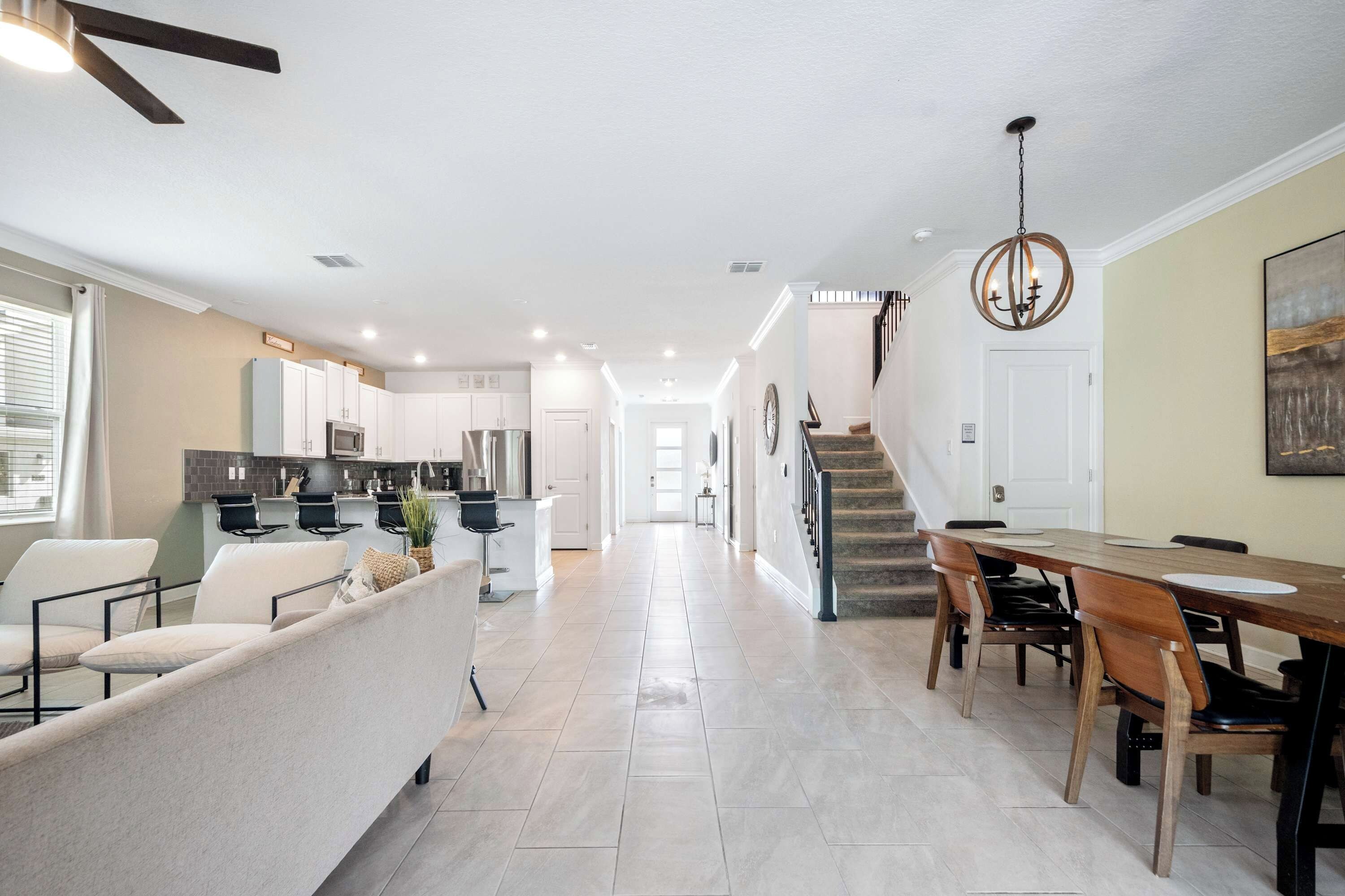 A spacious living area with a sofa, dining table, and chairs. A kitchen is visible in the background with cabinets and appliances.