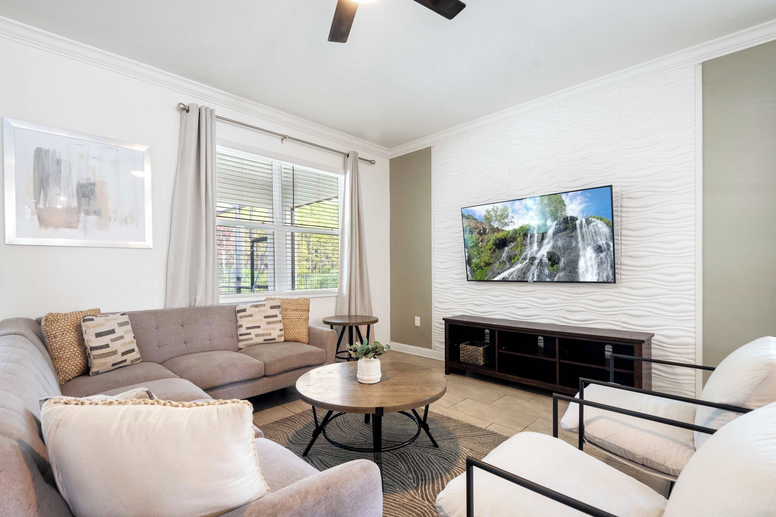 A modern living room with a sectional sofa, a round coffee table, and a flat-screen TV mounted on the wall.