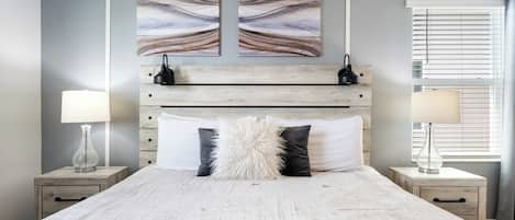 A bedroom with a large bed, two nightstands, a wooden headboard, and abstract wall art.
