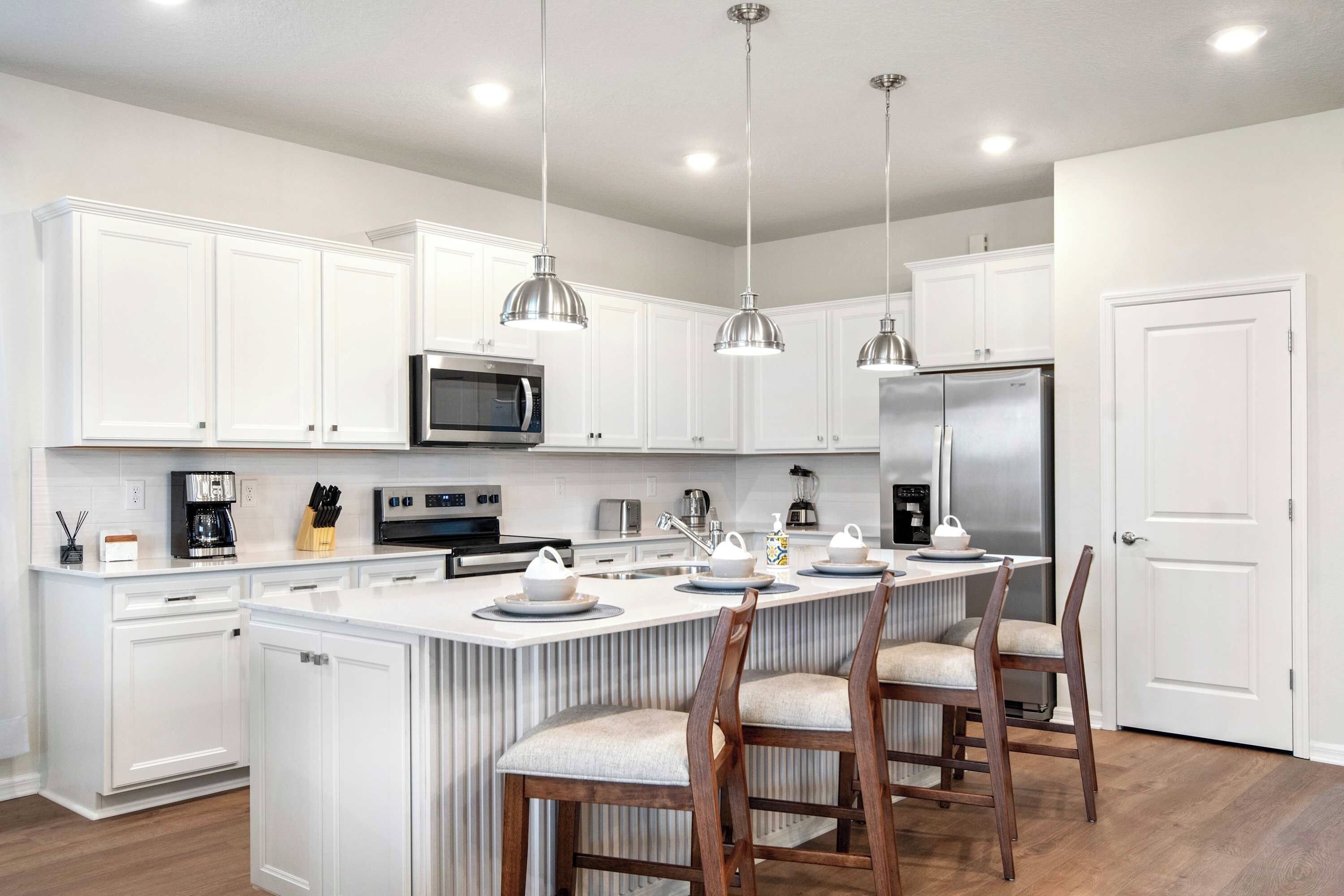Una cocina moderna con armarios blancos, electrodomésticos de acero inoxidable y una isla central con taburetes de bar.