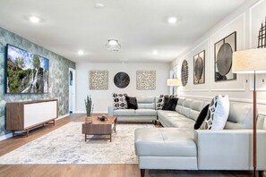 A modern living room with a sectional sofa, a coffee table, and a TV mounted on the wall. - Resort Access/7br Family-villa/close2parks! (Clermont)