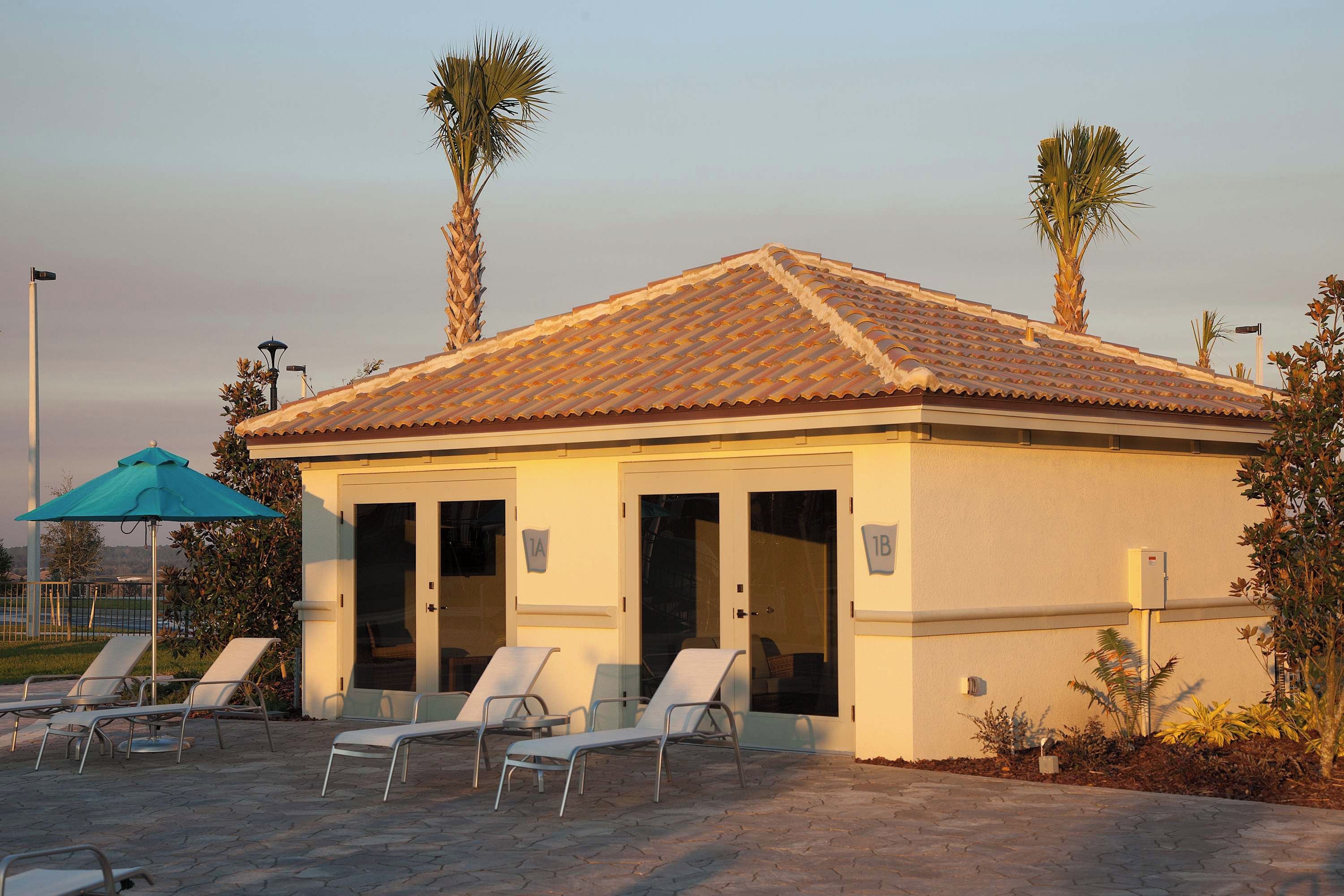 Een gebouw met een pannendak, een overdekt terras met lounge fauteuils, en palmbomen.