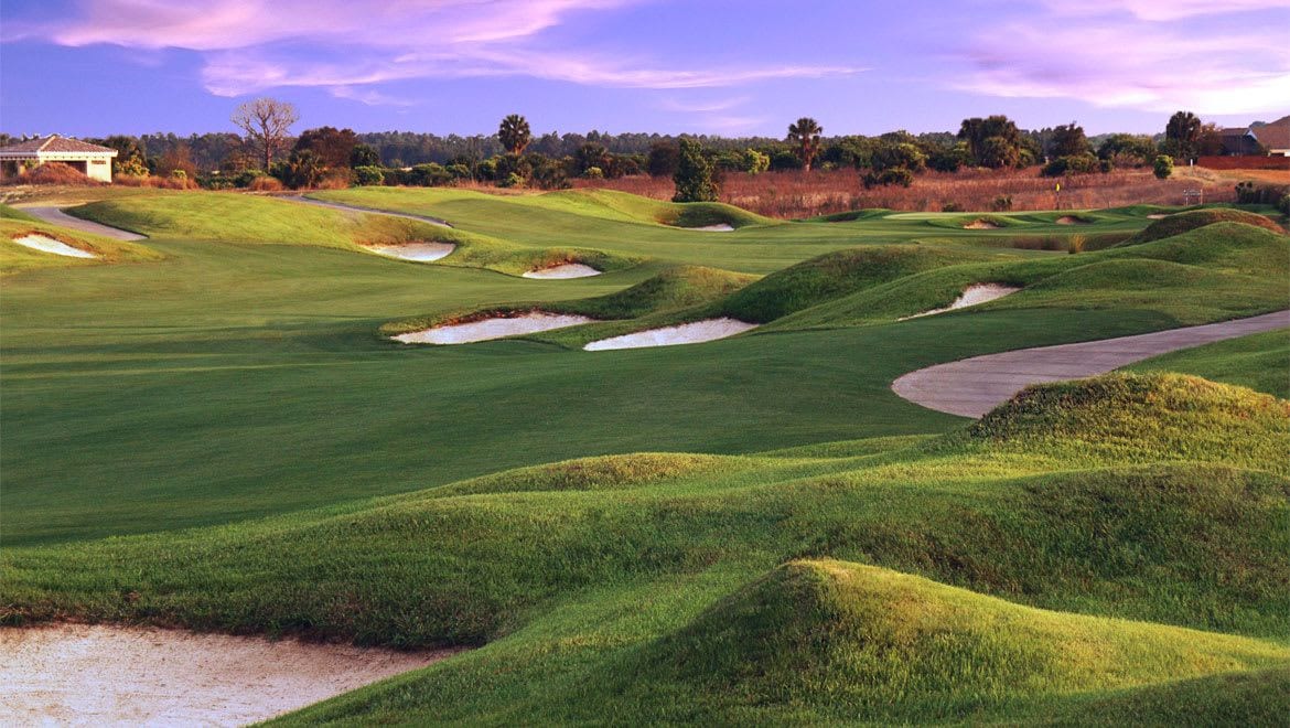 Um campo de golfe com bunkers de areia, um clube de campo e céu limpo.