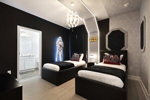 Une chambre avec deux lits, une décoration sur le thème de Star Wars, un lustre et une vue sur une autre pièce.