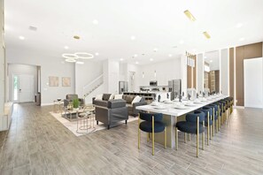 A spacious living area with a long dining table, modern furniture, and a staircase leading to an upper level. - Avatar Gameroom/theater/resort Access/huge 15br! (Kissimmee)