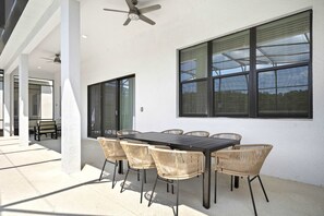 An outdoor patio with a rectangular table and six wicker chairs, large windows, and ceiling fans. - Avatar Gameroom/theater/resort Access/huge 15br! (Kissimmee)