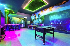 Une pièce équipée d’une table de billard, d’un baby-foot et ornée d’une fresque représentant un paysage fantastique.