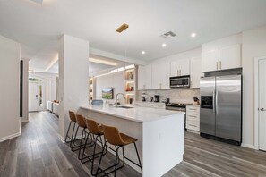 Eine moderne Küche mit einer zentralen Kochinsel, Barhocker, Edelstahlgeräten und einem klaren, minimalistischen Design.