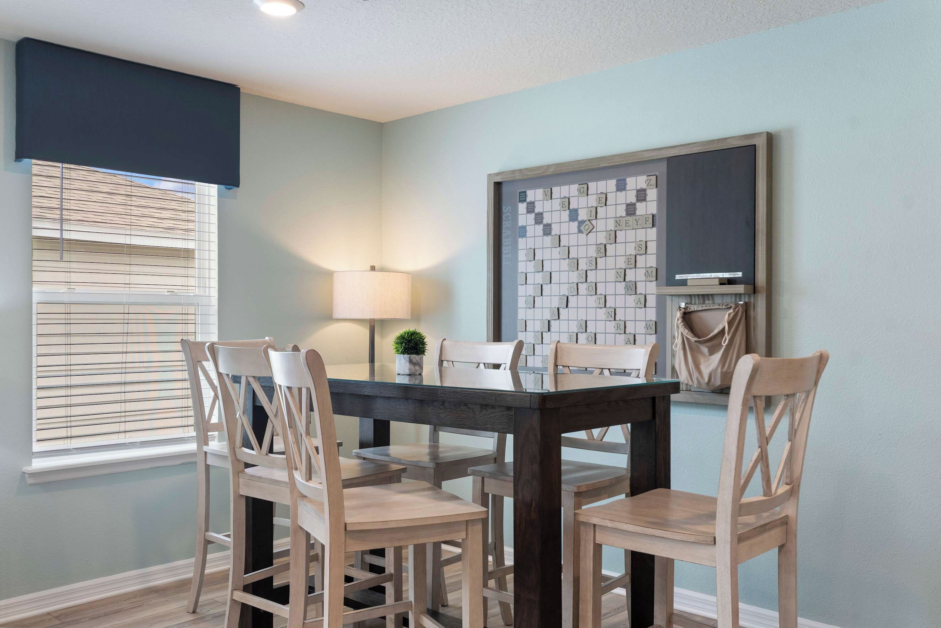 Un coin repas avec une table et des chaises, une fenêtre avec des stores, une lampe et une œuvre d’art encadrée accrochée au mur.