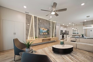 A modern living room with a sofa, a coffee table, a TV mounted on the wall, and a ceiling fan. - NEW Mario World Private Pool Near Clubhouse (Davenport)