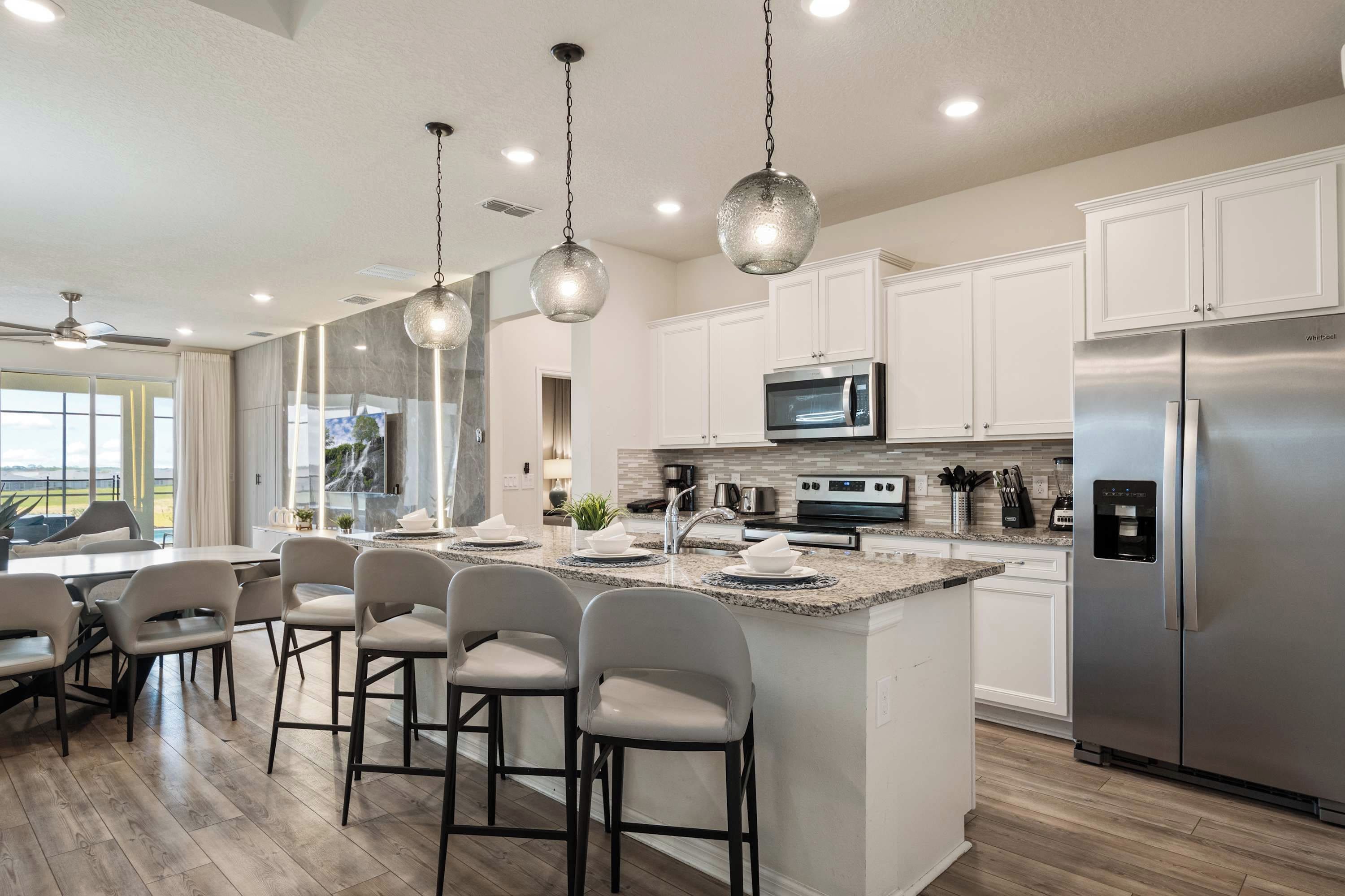 A modern kitchen with white cabinets, stainless steel appliances, and a bar area with stools.