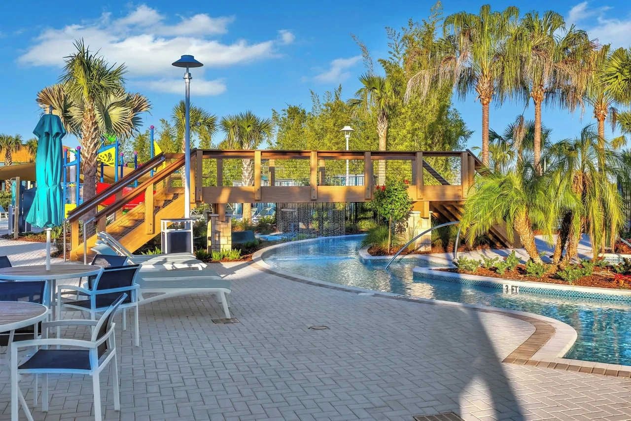 Un área de piscina con un puente, palmeras y mobiliario exterior.