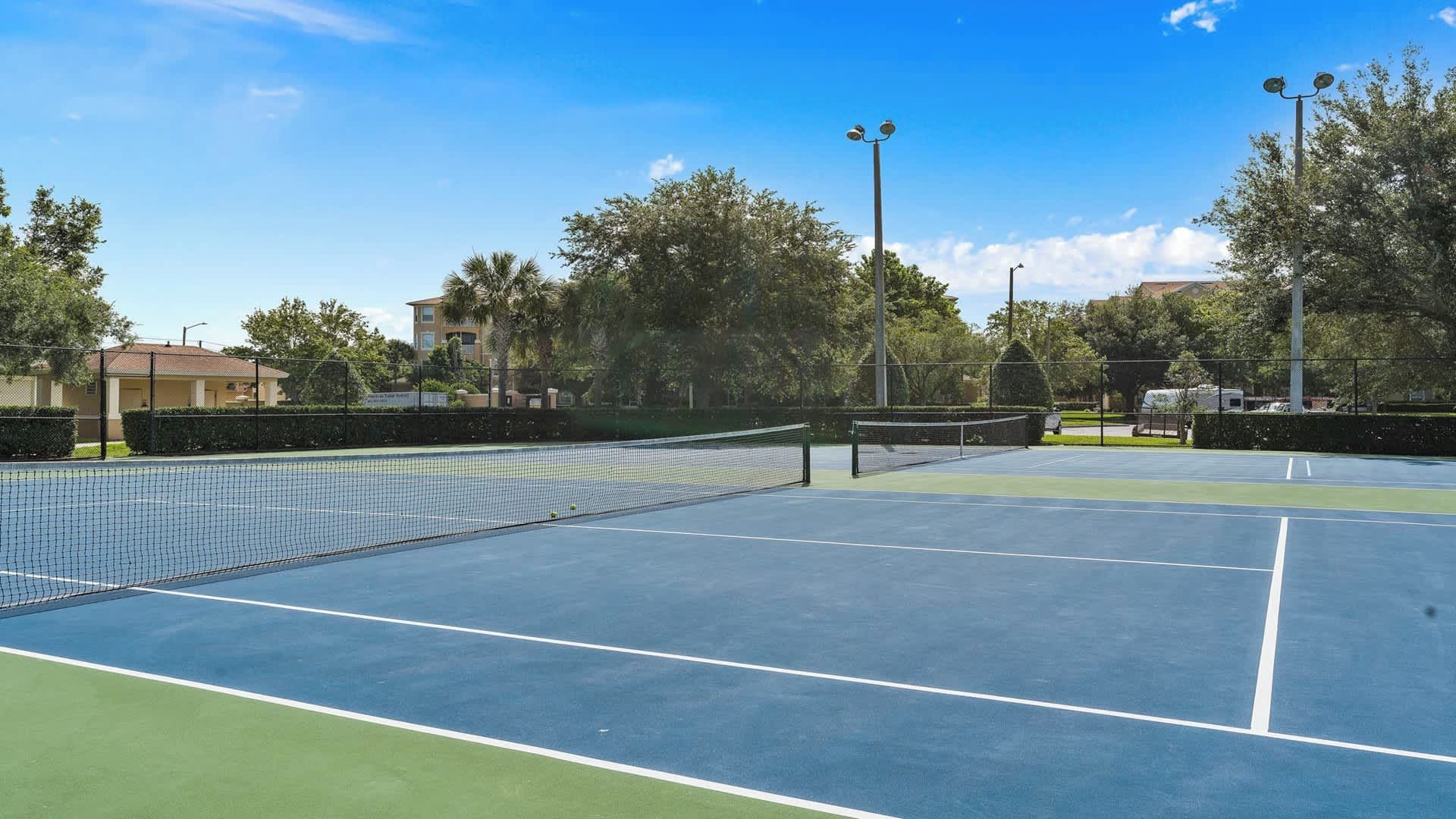 An outdoor tennis court with a net, surrounded by trees and a fence.