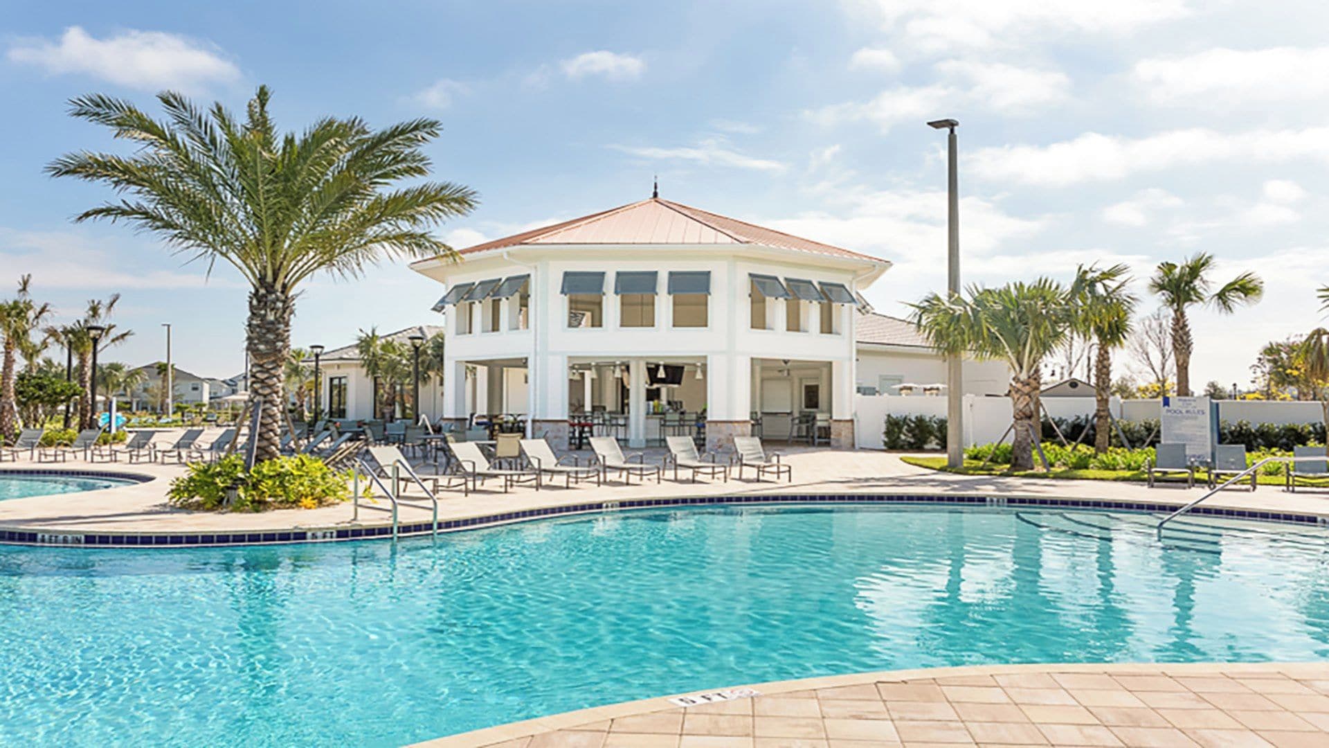 A pool area with lounge chairs and a building with a red roof.