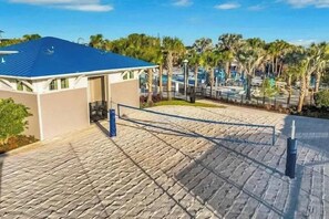 Un hotel amb teulada blava, passatge pavimentat i palmeres al fons.