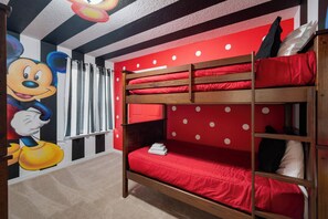 Ein Mehrbettzimmer mit roter Bettwäsche, einer Wandmalerei mit Mickey Mouse und einem Streifenvorhang.