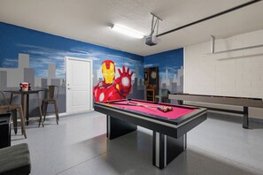 Taula de bitlles amb feliçó vermella, un joc de daus i un mural de l'Iron Man a la paret.