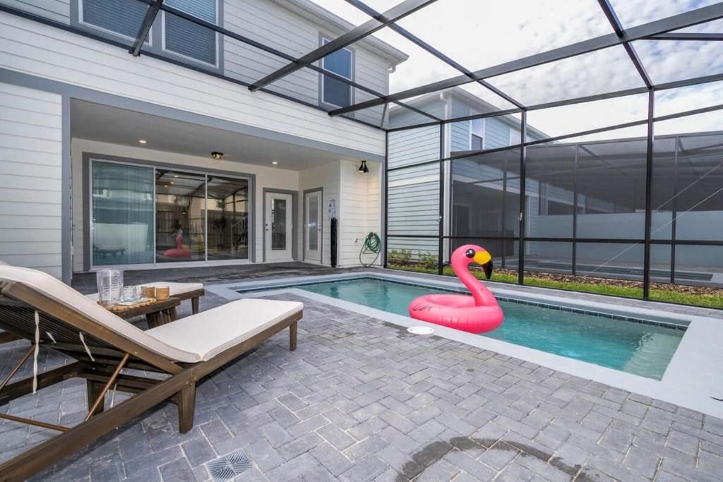 A modern house with a glass-enclosed patio, a swimming pool, and a pink flamingo inflatable.