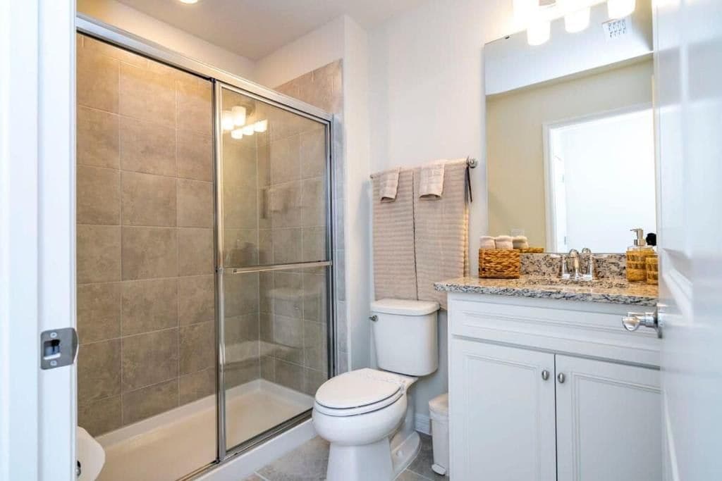 A modern bathroom with a glass-enclosed shower, a toilet, and a vanity with a mirror and countertop.