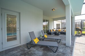 A covered outdoor seating area with lounge chairs and a sofa, a door with a glass panel, and a view of a swimming pool. - Enchanted Palms Villa 7BR w Private Pool (Davenport)