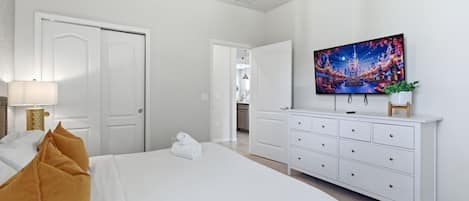 Quarto de hotel com uma cama, televisão, penteadeira e porta.