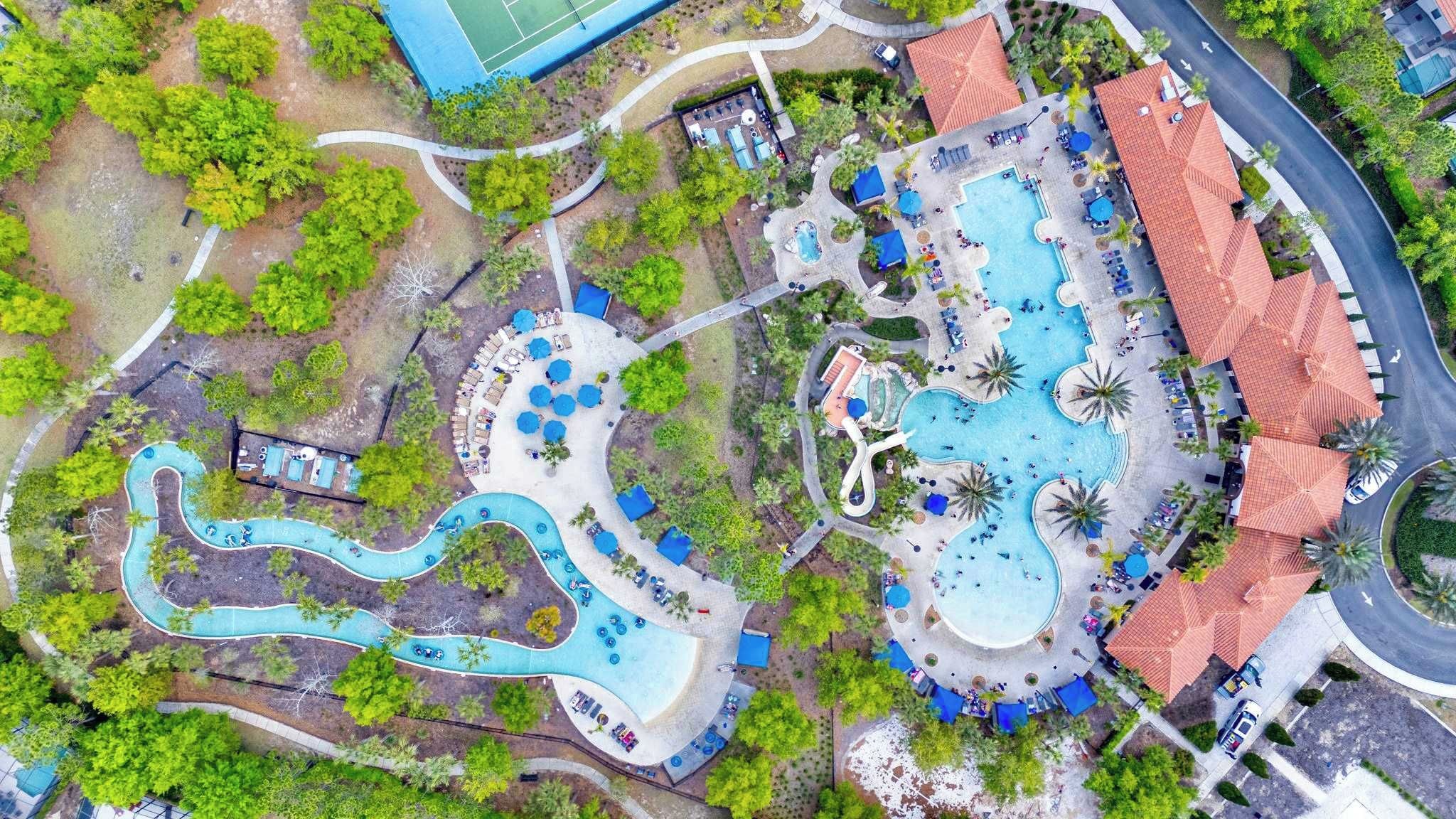 An aerial view of a resort with multiple swimming pools, a winding water slide, and a variety of outdoor seating areas.
