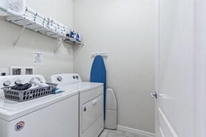 A laundry room with a washing machine, dryer, ironing board, and a basket of clothes. - Enchanted Palms Villa 7BR w Private Pool (Davenport)
