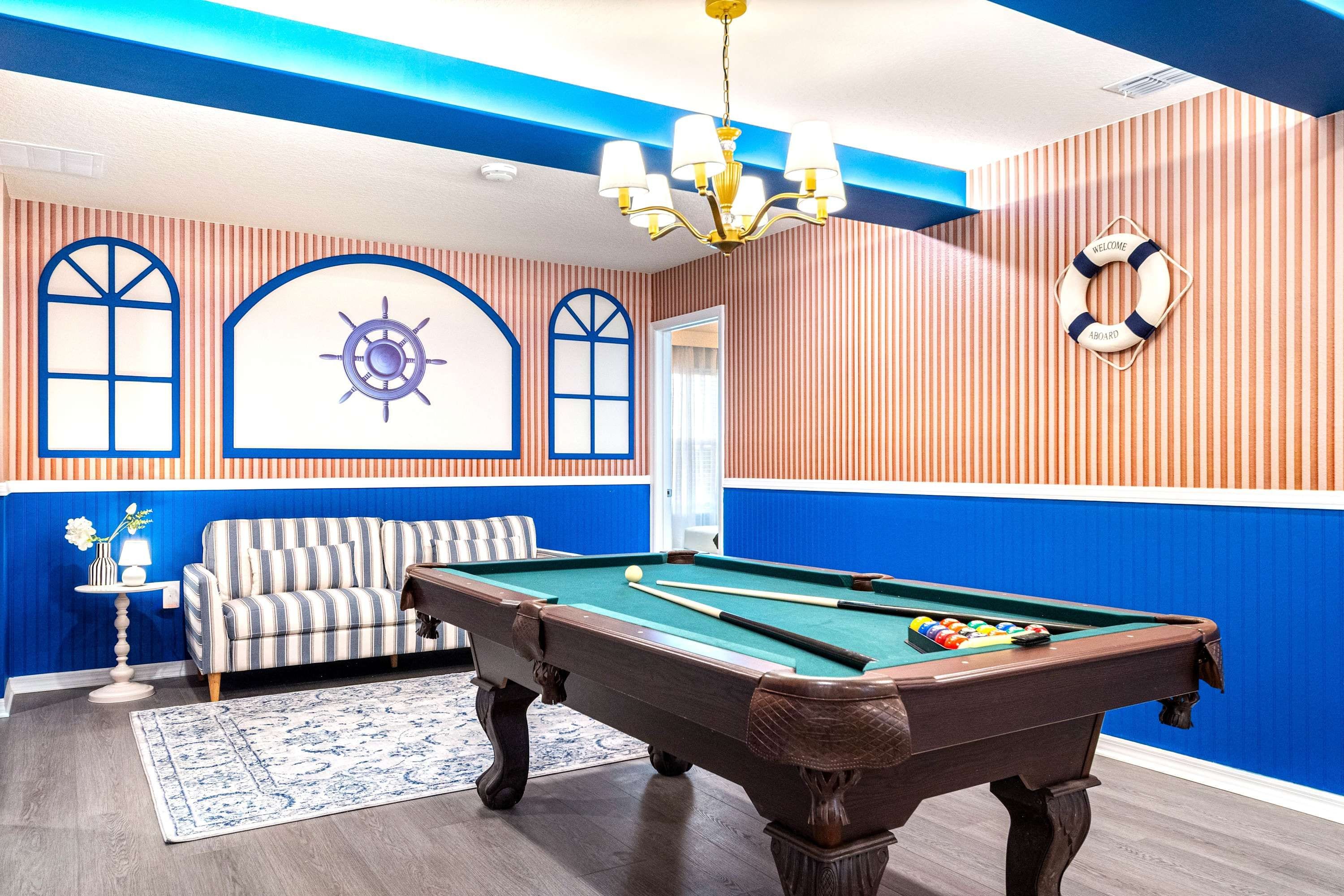 A pool table in a room with striped walls, a sofa, and a chandelier.