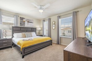 Une chambre à coucher avec un lit, un bureau, un ventilateur de plafond et un téléviseur.