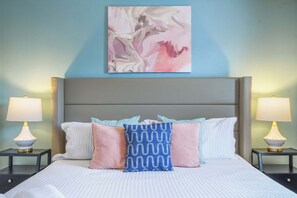 Een hotelkamer met een groot bed, twee bedlampen, een hoofdeinde en een abstract schilderij aan de muur.