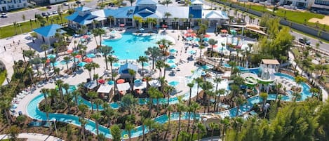 An aerial view of a resort with multiple swimming pools, palm trees, and a central building with a blue roof.