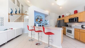 Eine moderne Küche mit einer zentralen Kochinsel, Barhocker, einem Kühlschrank, einer Mikrowelle, einem Herd und Holzausbau.