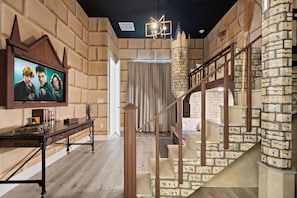 A room with a stone wall, a wooden staircase, and a television on a wooden table. - Lake View 15br Villa w Pool, Spa & Games Near Parks (Kissimmee)