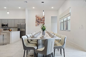 A modern dining area with a long table set for a meal, surrounded by chairs. - Lake View 15br Villa w Pool, Spa & Games Near Parks (Kissimmee)