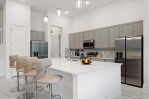 A modern kitchen with a central island, stainless steel appliances, and bar stools. - Lake View 15br Villa w Pool, Spa & Games Near Parks (Kissimmee)