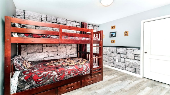 Una cama litera con un edredón estampado, un banco de madera y una pared de piedra.