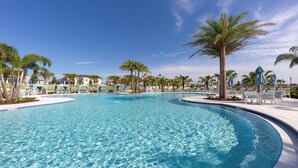 Una piscina amplia y cristalina rodeada de palmeras y sillones de descanso.
